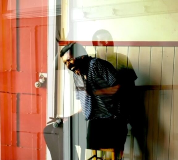 A person appears to be screaming or yelling as they sit on a chair in front of a yellow wall. There is a read door to the left and the image appears to be overlapped with another.