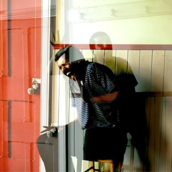 A person appears to be screaming or yelling as they sit on a chair in front of a yellow wall. There is a read door to the left and the image appears to be overlapped with another.