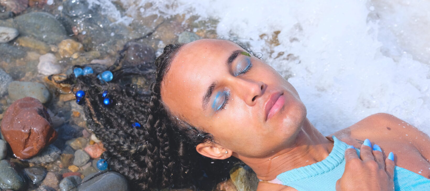 A film still of someone wearing a light blue top, lying on some rocks by the ocean.