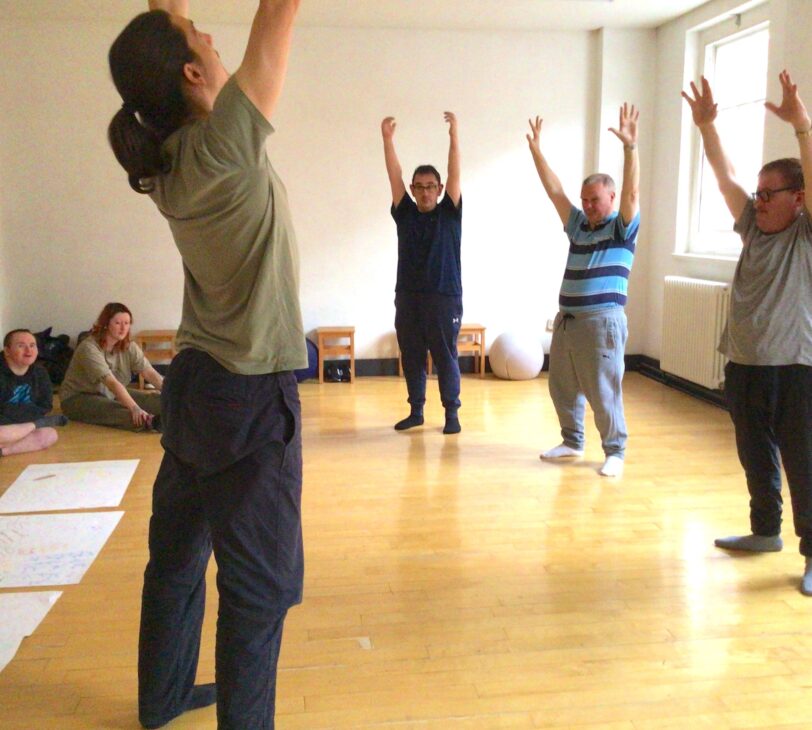 Image shows artist Willie Dickie with Blue Room artists in the dance studio. They all have their hands raised above their heads and are stood in a circle.