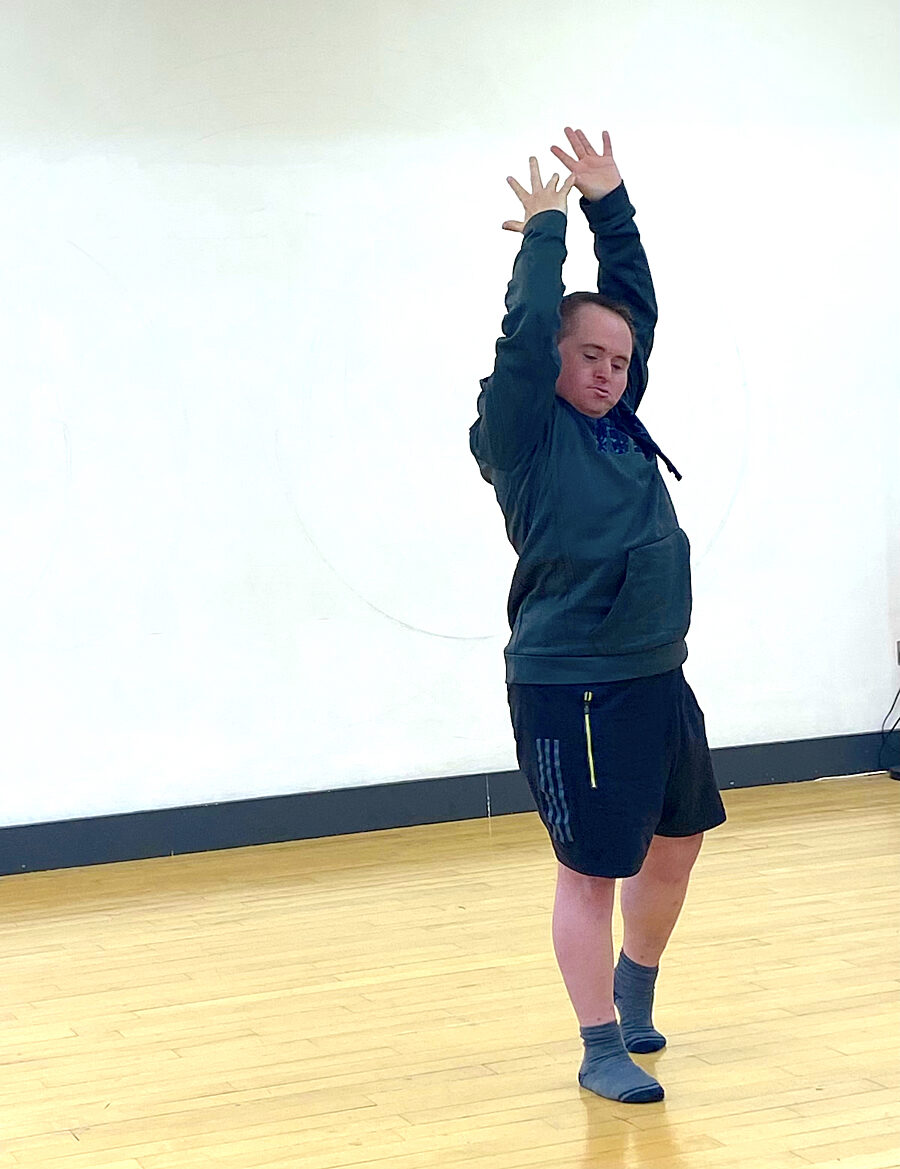 Image shows Blue Room artist Tony Carroll in a dance studio. He is wearing a blue jumper and black shorts and has his arms raised above his head with his eyes closed.