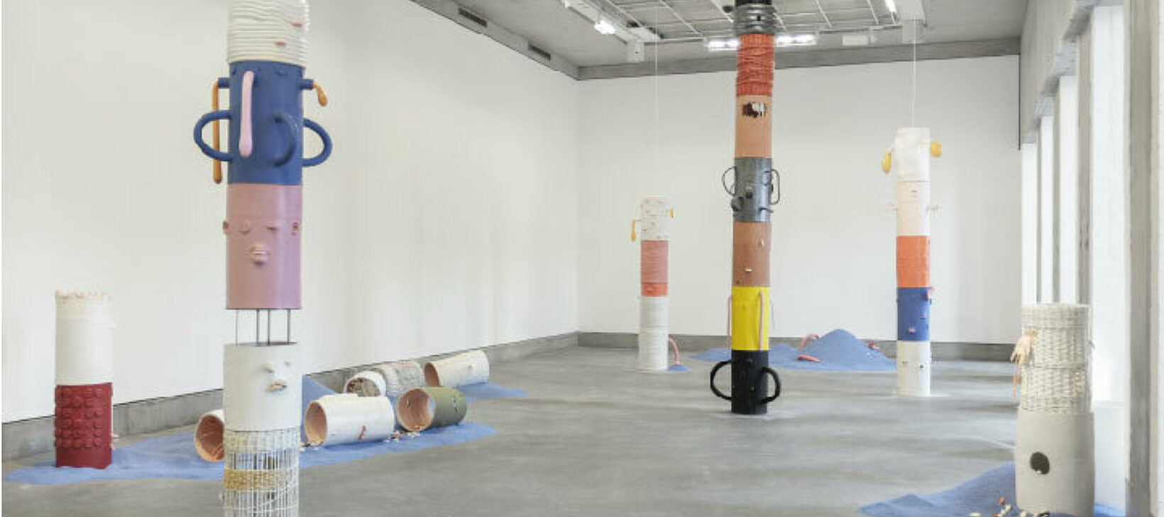 A photograph showing Jonathan Baldock's exhibition Facecrime. The image shows a collection of sculptural works; multicoloured ceramic columns with different expressive faces on them.