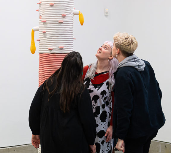 Three people look up towards a large pink and white sculpture by Jonathan Baldock in Bluecoat's Gallery.