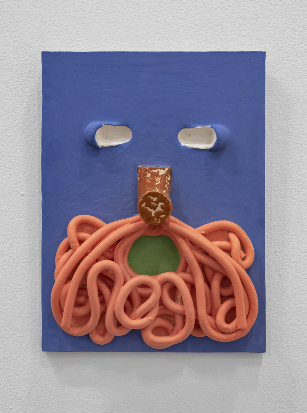A photograph of a work by Jonathan Baldock. The piece is a dark blue ceramic face. The face has a orange beard and a shocked expression.