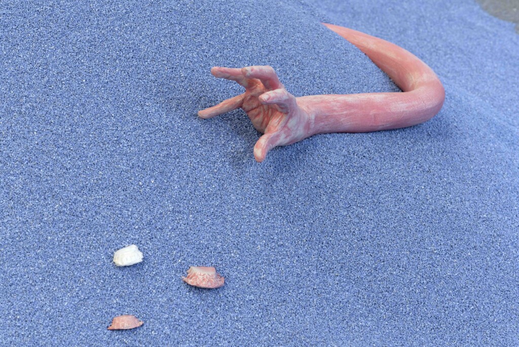 A close-up shot of a piece by Jonathan Baldock. The image shows a mound of blue rubble, with a pink ceramic arm protruding out of it, reaching for some ceramic fragments.