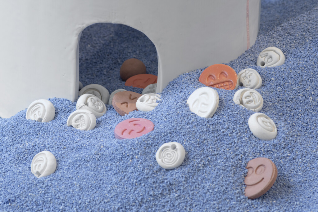 A close-up shot of a piece by Jonathan Baldock. The image shows a mound of blue rubble, populated by multicoloured disks with different emoji expressions on them.