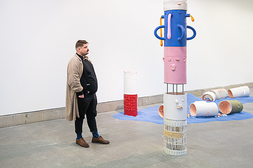 A photograph showing Jonathan Baldock's exhibition Facecrime. The image shows a visitor looking at a large ceramic sculpture, which is blue, pink and white.