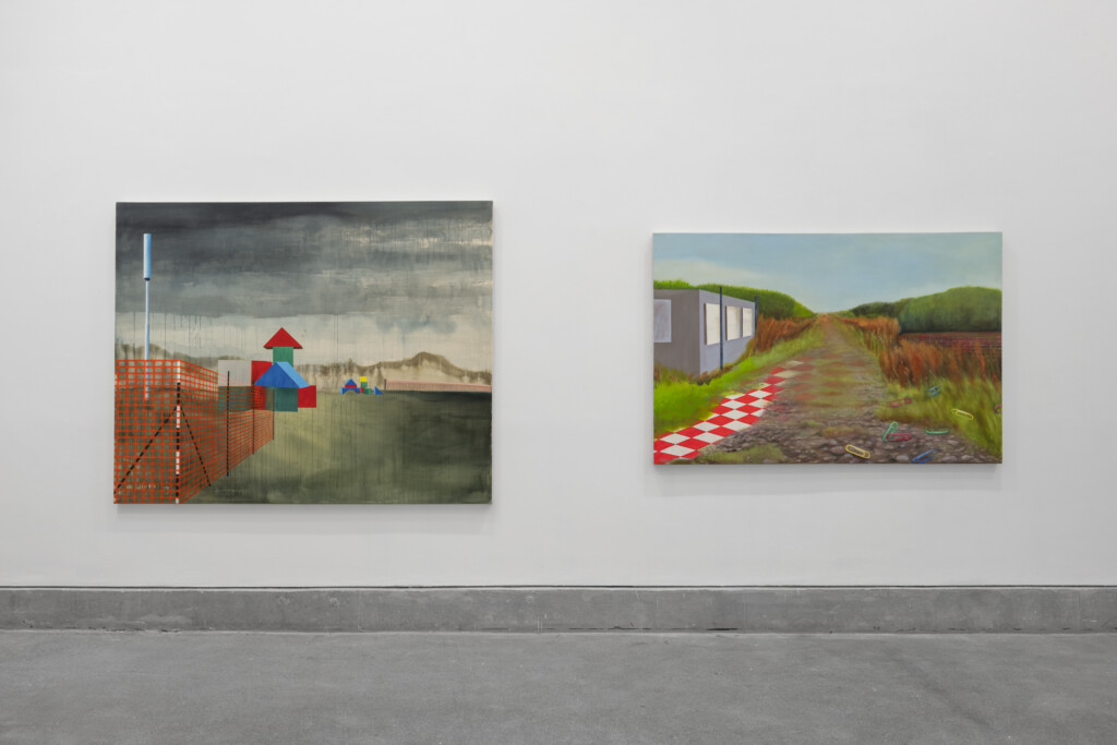 A photograph of the inside of Josie Jenkins' exhibition, Assembled Worlds. The photo shows two landscape paintings, one a murky scene with children's building blocks, the other a green landscape with a grey building.