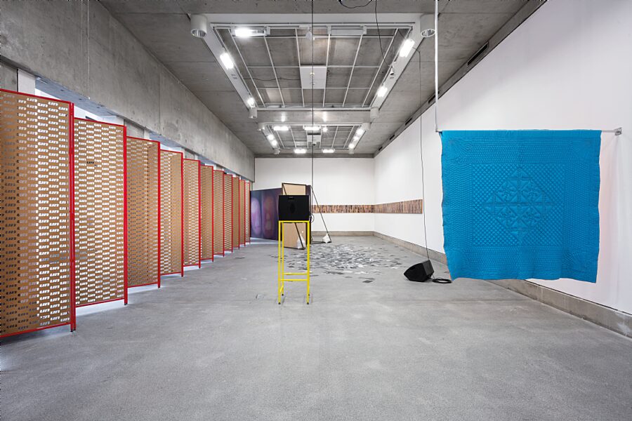 An installation view of Undo Things Done, featuring a blue quilt hanging from the wall at the foreground.