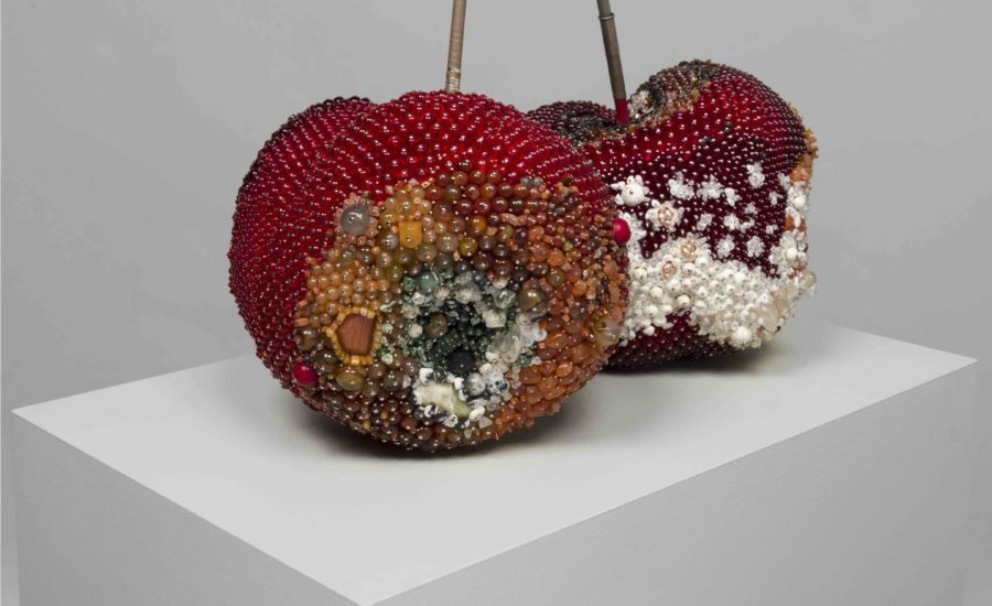 Two large sculptures resemble red cherries are sat on a white plinth. The artwork appears to be made out of colourful rhinestones.