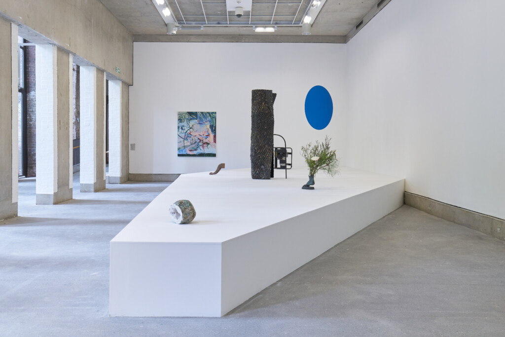 A collection of seven sculptural works by Andre Romao on a large plinth, including a blue circle hanging from the ceiling.