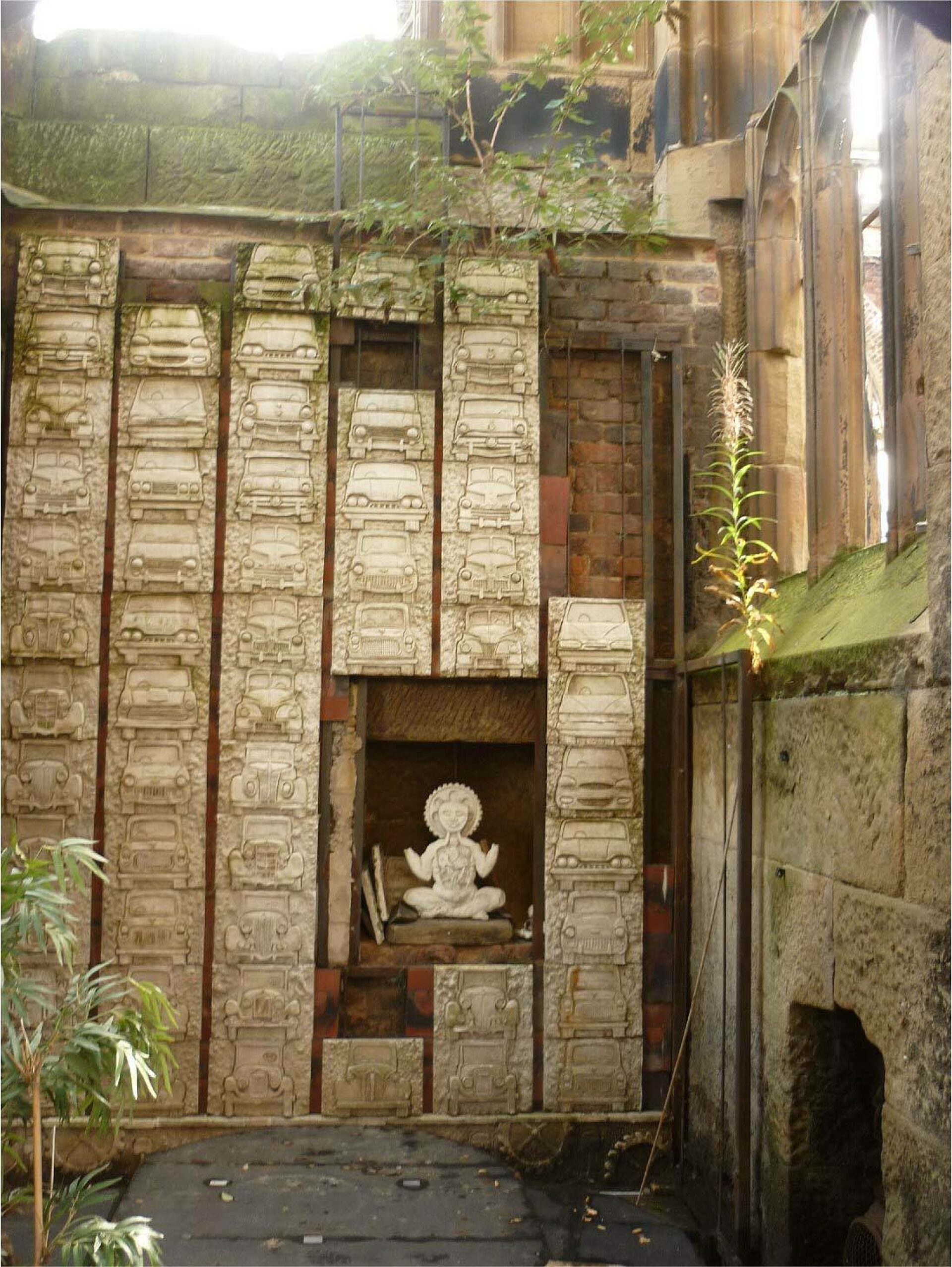 An installation at Liverpool's Bombed out church shows stacks of boxes which appear to be carved in stone, with green plants above and to the side.