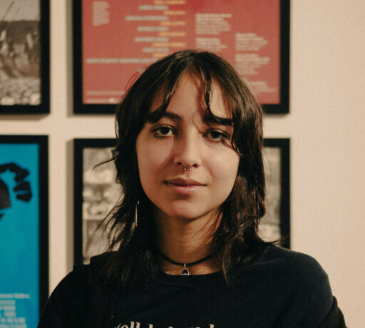 Image is a portrait photo of Shanti. She is wearing a black tshirt that has the text 'well behaved women barely make history.', a black necklace and has black short hair.