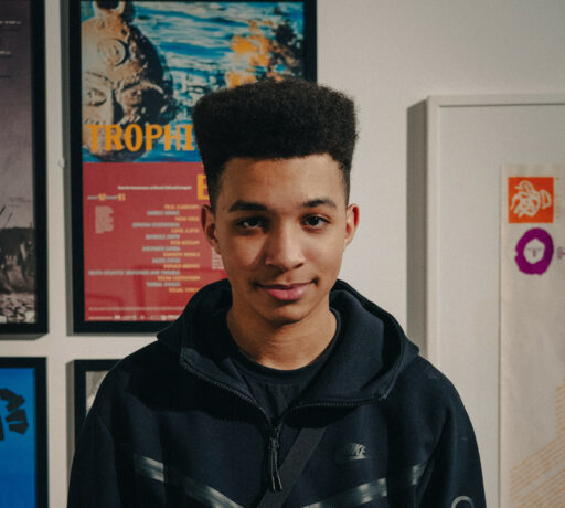 Image is a portrait of Kaidyn in the gallery. He is look straight at the camera smiling. He is wearing a black jacket and has black hair.