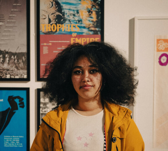 Image shows Tia Hume-Jennings. She has black hair and is wearing a yellow/orange coat with a white tshirt.