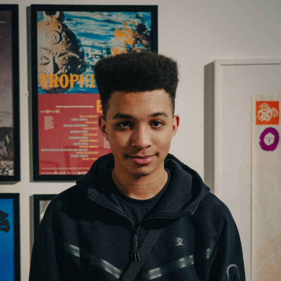 Image is a portrait of Kaidyn in the gallery. He is look straight at the camera smiling. He is wearing a black jacket and has black hair.