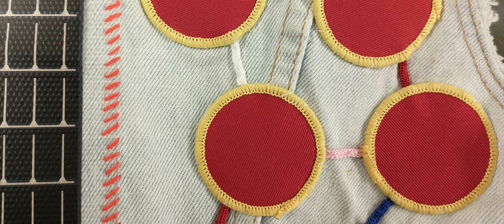 A close up of a jacket that contains various patches and stitches. The primary pattern is four red circles with yellow rims, attached in a network style.