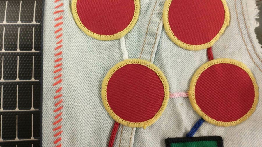 A close up of a jacket that contains various patches and stitches. The primary pattern is four red circles with yellow rims, attached in a network style.