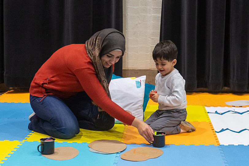 A mother and child play on a blue, yellow and orange coloured floor.
