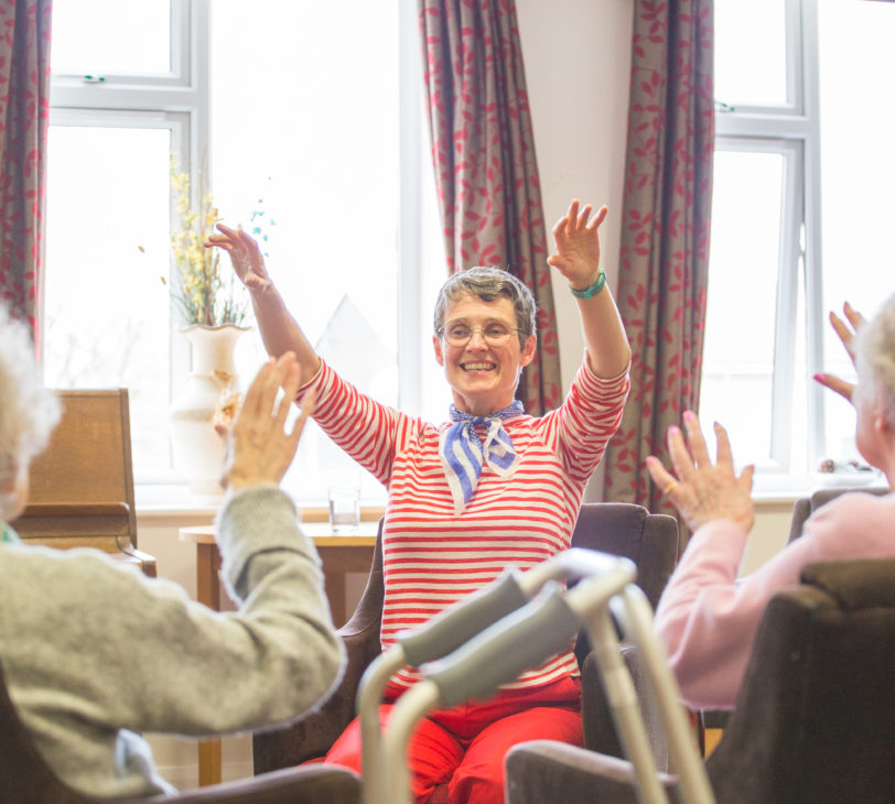 Three people, one is facing the camera and smiling with their arms in the air, and wearing a red striped top, the other two have their back towards the camera, are also raising their hands.