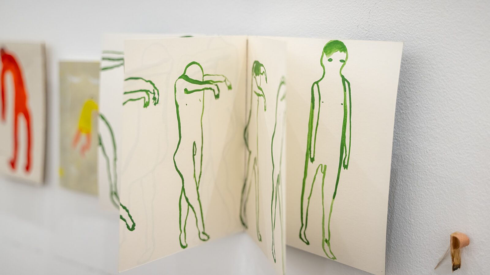 A small book has been hung on the wall. You can see images on various pages, showing small line drawings of green figures.
