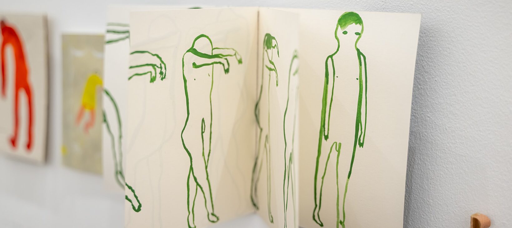 A small book has been hung on the wall. You can see images on various pages, showing small line drawings of green figures.