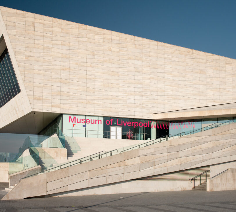 The exterior of a white building with 'Museum of Liverpool' written in pink, in front of blue skies.