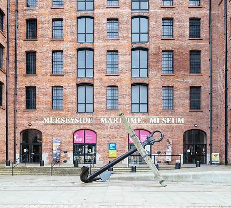 A photograph of a red brick building with the words 'Merseyside Maritime Museum' in white, and a giant black anchor in front.