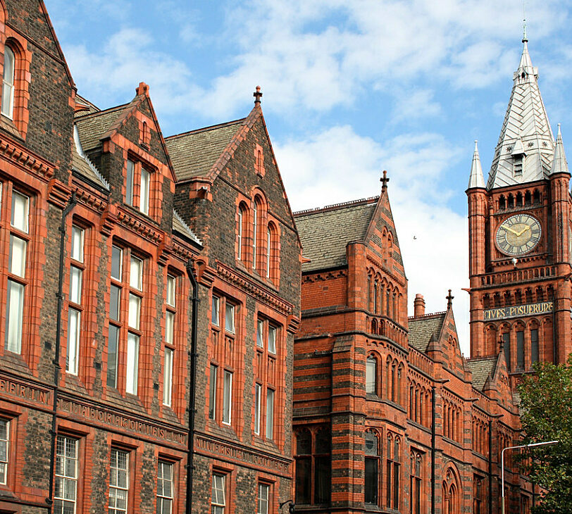 A photograph of a red brick building with a pointed clock tower on the right.